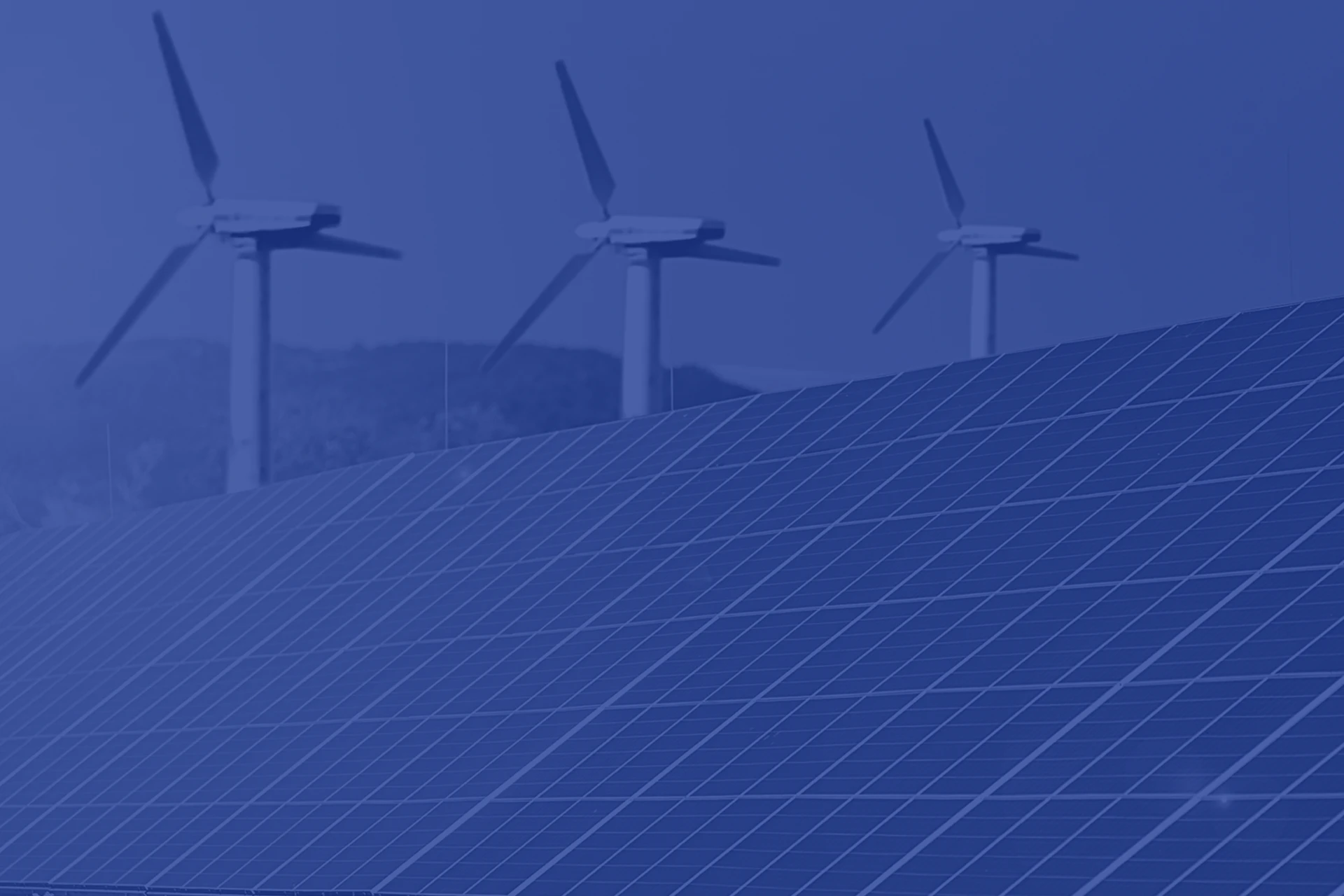 Imagen de un primer plano de una instalación fotovoltaica de placas solares y de fondo tres molinos de viento de energía eólica